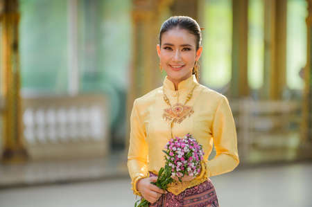 Attractive Thai woman in an ancient Thai dress holds a fresh flowers paying homage to Buddha to make...