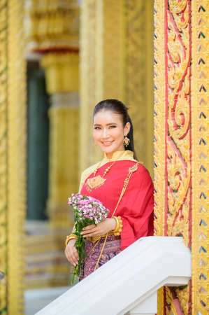 Attractive Thai woman in an ancient Thai dress holds a fresh flowers paying homage to Buddha to make a wish on the traditional Songkran festival in Thailandの写真素材