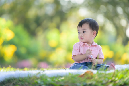 Asian boy sitting on the carpet holding a pen while learning from outside the school in the nature...