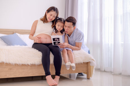 An Asian family, parents and daughters are watching an ultrasound film of a child in their mother's womb happily approaching the time of deliveryの写真素材
