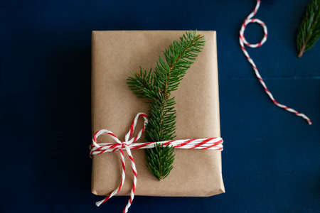 woman wraps a handmade eco style christmas present in kraft paper and natural spruce branches on a blue wooden backgroundの写真素材