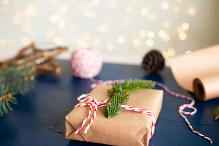 woman wraps a handmade eco style christmas present in kraft paper and natural spruce branches on a...