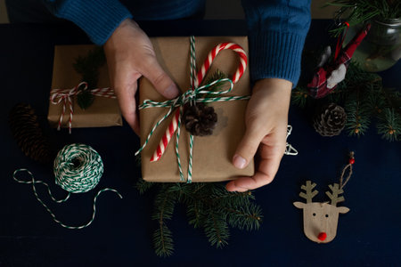 man wraps a handmade eco style christmas present in kraft paper and natural spruce branches on a blue wooden backgroundの写真素材