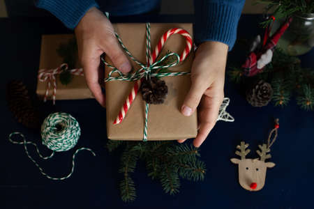 man wraps a handmade eco style christmas present in kraft paper and natural spruce branches on a...