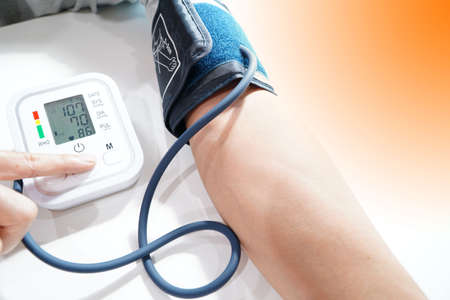 Monitoring blood pressure of patients using upper arm blood pressure monitor in the clinic examination room.の写真素材