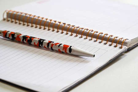 Spiral notepad and pen placed on wooden desk. Close up.