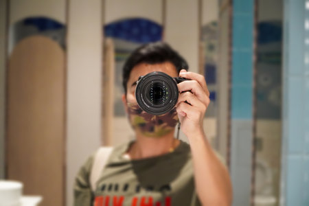 Young man taking pictures with his camera looking through the viewfinder from the bathroom mirror.Person pointing a camera lens at youの写真素材