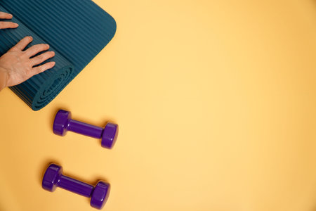 fitness accessories concept.Purple dumbbell sport with blue yoga mat on orange background, Copy...