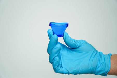 Male hand in blue medical glove holding eye wash cup isolated on white background.irritated and uncomfortable eyes.eye wash stationの写真素材