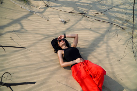 Beautiful young woman in a black top and red pants posing on the beach in the sand dunes.の写真素材