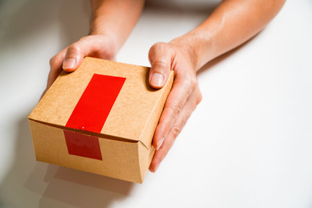 Man's hand holding a cardboard box with a red sign,Isolated on Grey studio Background. Copy Space.の写真素材