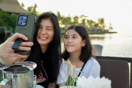 Mother and two Asian daughters take a selfie with their cell phones on a boat in the tropical sea.の写真素材