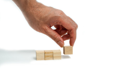 Man's hand placing wooden cube on white background, business concept.