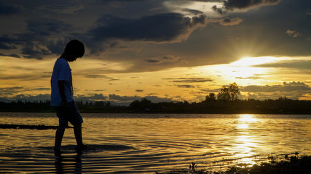 silhouette of asian boy playing in the water at sunset.Thaiの写真素材