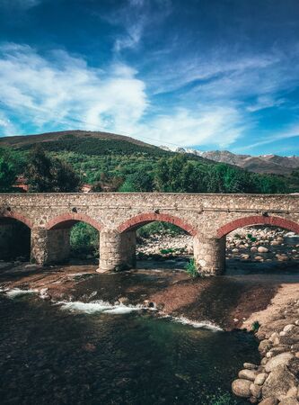 Old roman bridge next to a river and some green mountains and a little snowfall, Candeleda, Avila.の写真素材