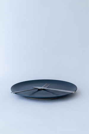 Stylish tableware composition with blue plate, fork, and knife. Clean white background and soft...
