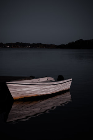 A peaceful evening view of a white boat moored near a pier, reflecting the golden light of sunset on the calm water.の写真素材