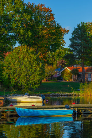 Autumn day at the lakeside with two boats resting near a wooden pier and a cozy house in the background.の写真素材