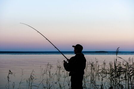 Fisherman silhouette at sunset on the lake while fishingの写真素材