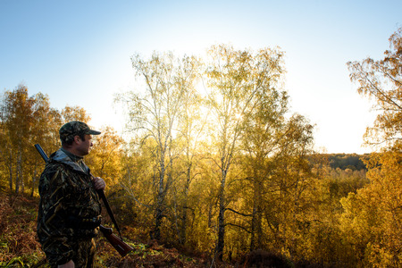 A hunter with a gun in the forest at dawn.の写真素材