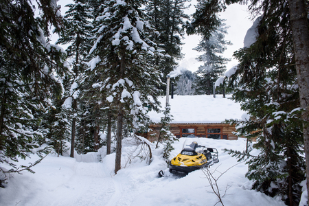 A snowmobile is standing by a wooden house in the forest, smoke is coming from the pipeの写真素材