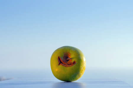 Ripe fresh green apple on blue board and summer sunset sea background. Summer or autumn concept. Smile apple. Copy space.の写真素材