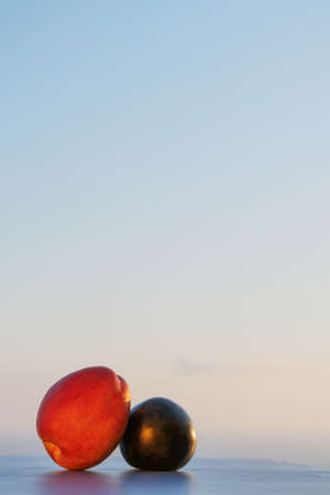 Fresh red peach and black plumb on blue board and summer sunset sea background. Mediterranean summer or autumn concept. Space for text. Copy space. Vertical photo. Summer fruit and sky background.の写真素材