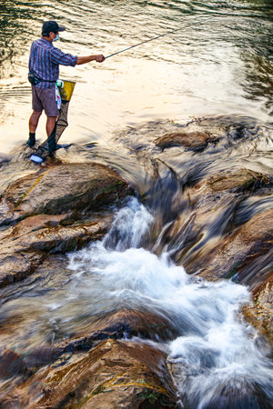 A fisherman concentrates on fishing by the riverの写真素材