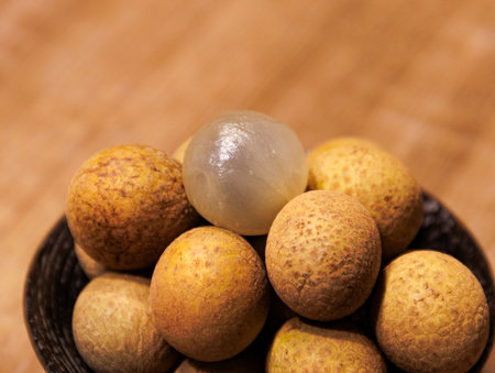 This is a close-up photo of some longan placed in a bowl. Most of the longan are brown and yellow,...