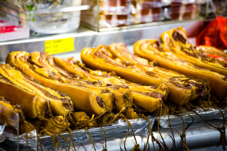 an array of traditional cured bacon with a golden hue and rich fat marbling at a market stallの写真素材
