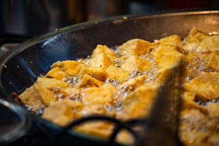 pieces of tofu are being deep-fried in a hot oil wok until golden and crispyの写真素材