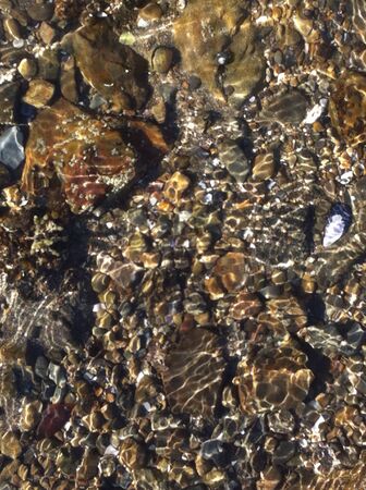 Light catches water moving over pebbles at beachの素材