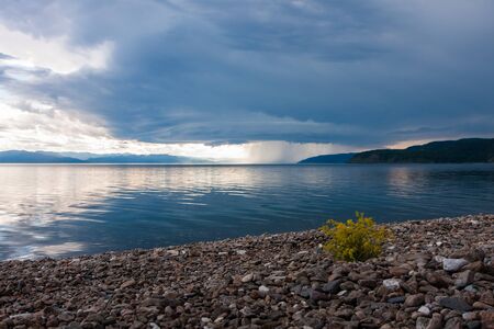 Storm with heavy rain and bright sun over the shore of lakeの写真素材