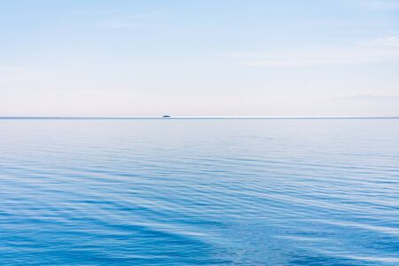 Light and simple landscape with blue sky, light clouds and wavy blue water with a shipの写真素材