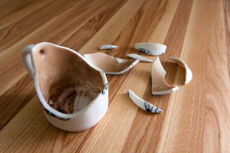 Broken white Cup with shards on a background of striped woodの写真素材