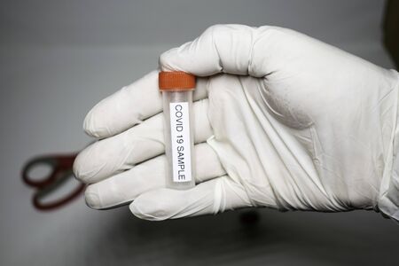 microbiologist with a tube of biological sample contaminated by Coronavirus with label Covid-19 / doctor in the laboratory with a biological tube for analysis and sampling of Covid-19 infectious diseasの写真素材
