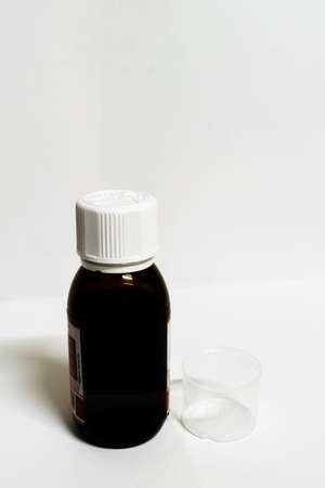 A medicine bottle with empty measurement cup in a white background with spaces for textの写真素材