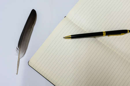 a pen and notebook with a feather on a white backgroundの写真素材