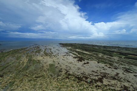 The view of rocky outcrop under thick clouds and blue sky during low tide at Pantai Bak Bak Beach in the District of Kudat in Sabah, Malaysia.の写真素材