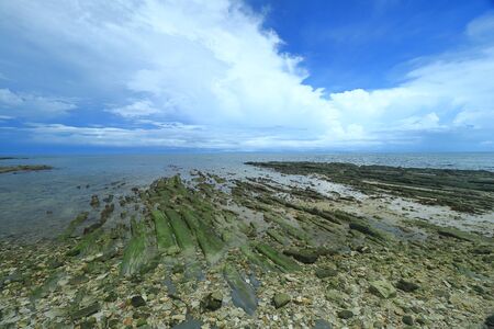 The view of rocky outcrop under thick clouds and blue sky during low tide at Pantai Bak Bak Beach in the District of Kudat in Sabah, Malaysia.の写真素材