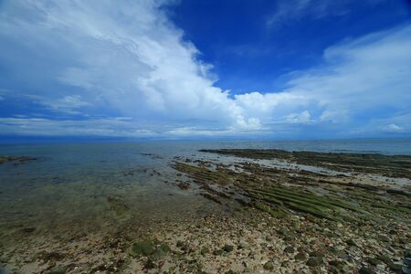 The view of rocky outcrop under thick clouds and blue sky during low tide at Pantai Bak Bak Beach in the District of Kudat in Sabah, Malaysia.の写真素材