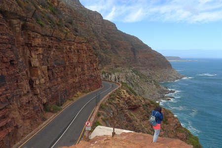 Chapman's Peak Dive, Cape Peninsula / South Africa - March 10 2020 : A woman at the Chapman's Peak Drive Lookout with the road that winds through steep cliff side above Atlantic Ocean.のeditorial素材
