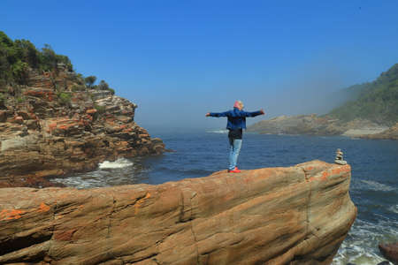torms River Mouth, South Africa - march 14 2020 : A woman stands on a boulder by the sea as she...