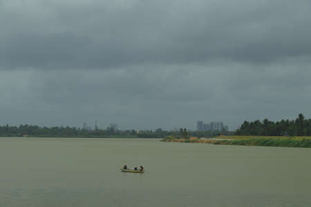 The Sungai Kelantan River with a small boat in it under cast, cloudy sky at the outskirt of the city of Kota Bharu in Kelantan, Malaysia.の写真素材