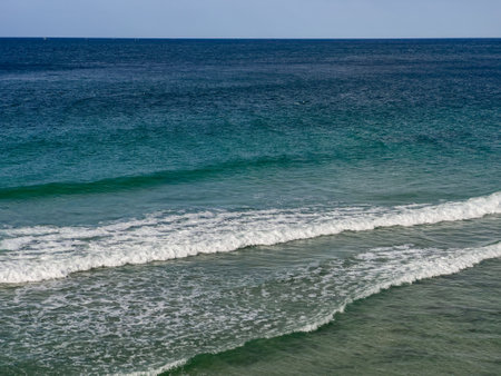 A stunning view of waves crashing against the white sand beach in Lamreh, Aceh. The sparkling blue...