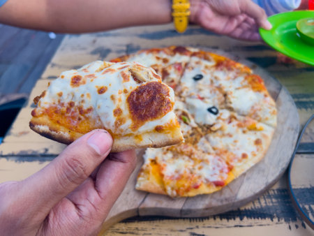 Chicken pizza with sausage and mushroom topping served on a wooden cutting board, placed on a wooden table at a beachside restaurant.の写真素材