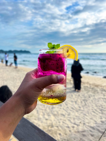 A cold and refreshing dragon fruit cocktail is held in hand at a restaurant located by the beach, perfect for enjoying and very refreshing.の写真素材