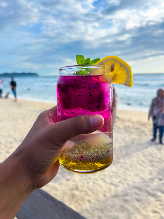 A cold and refreshing dragon fruit cocktail is held in hand at a restaurant located by the beach, perfect for enjoying and very refreshing.の写真素材