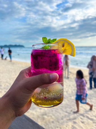A cold and refreshing dragon fruit cocktail is held in hand at a restaurant located by the beach, perfect for enjoying and very refreshing.の写真素材