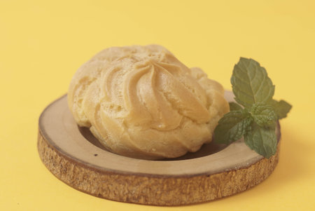 Kue Soes or choux Ã  la crÃ¨me isolated on a yellow background. Perfectly puffed and filled with a creamy filling, this classic French dessert is sure to delight. Selective Focus , Closeupの写真素材